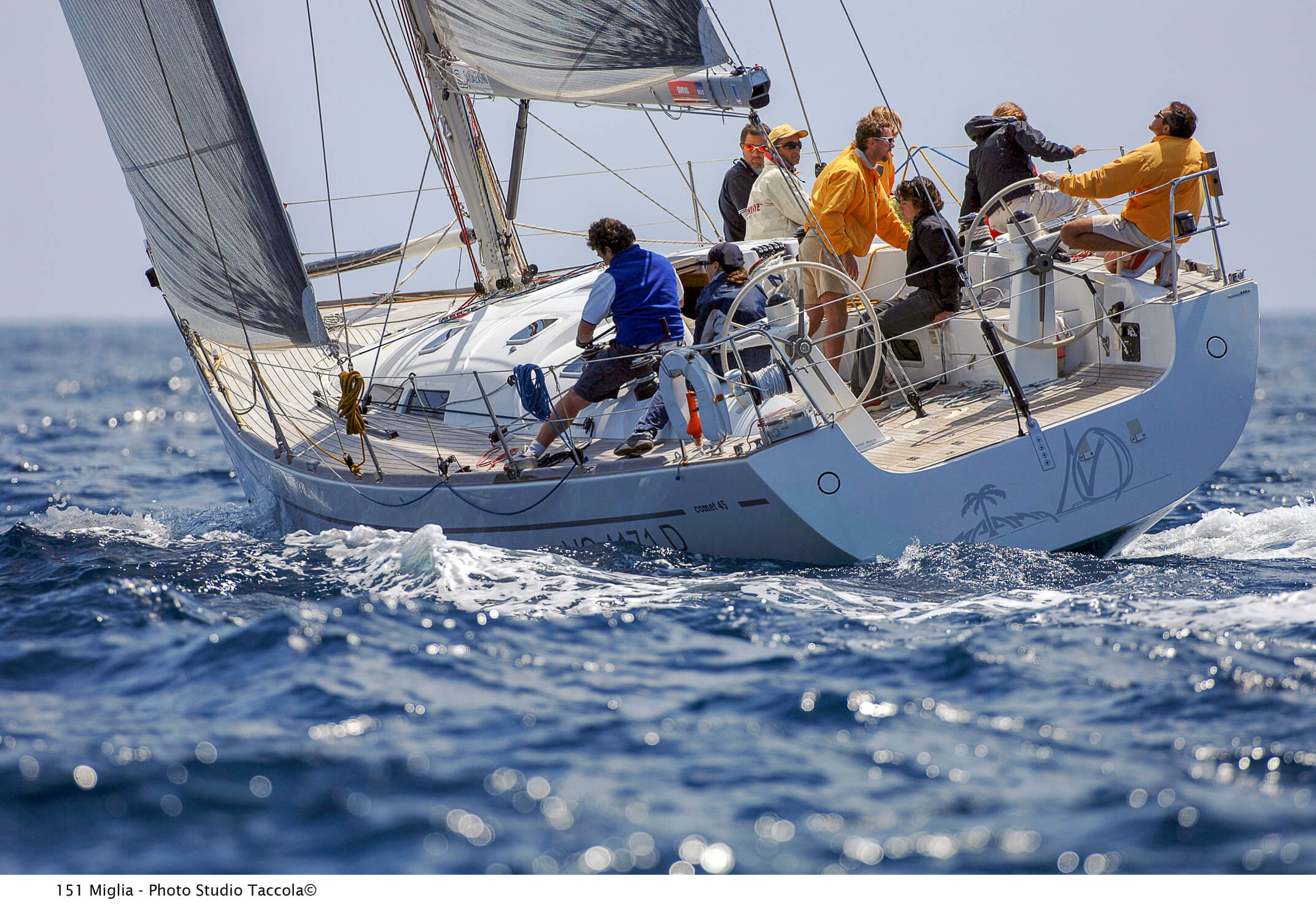 Equipaggio in navigazione su barca a vela da regata, con vele tecniche in film metallizzato.